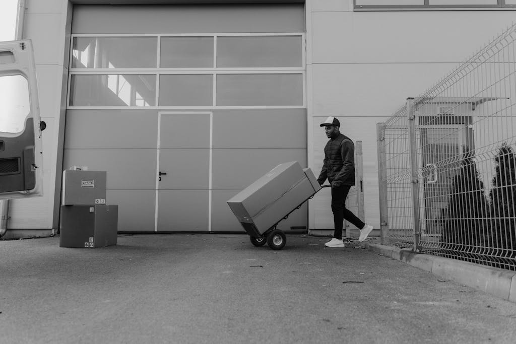 Black and white photo of a delivery worker moving packages outside a warehouse.